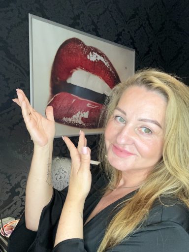 Frau mit langen blonden Haaren zeigt auf ein Kunstwerk mit roten Lippen.